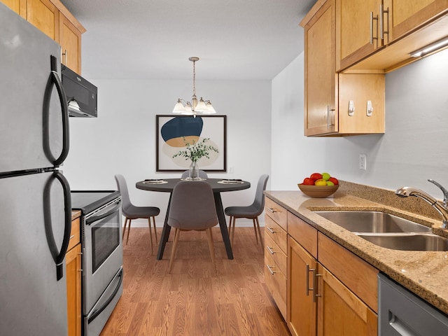 kitchen featuring light stone counters, light wood-style flooring, stainless steel appliances, a sink, and baseboards