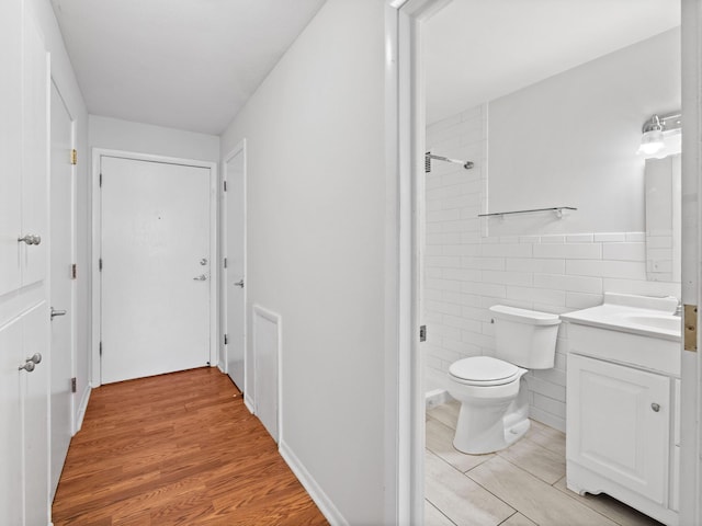 bathroom with tile walls, toilet, vanity, wood finished floors, and walk in shower