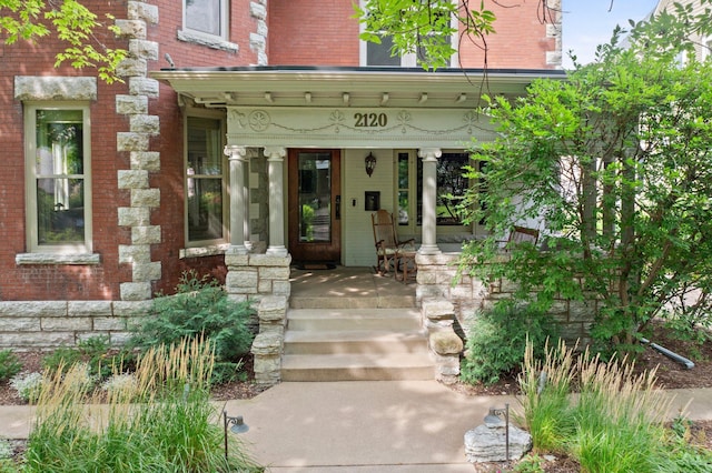 view of exterior entry with brick siding and covered porch