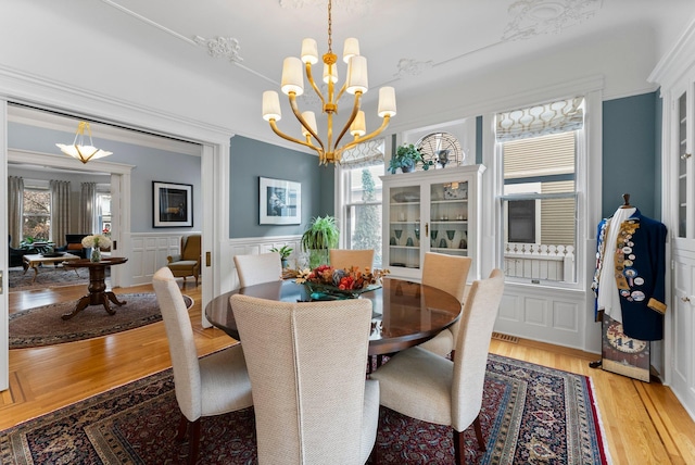 dining area featuring light wood-type flooring, ornamental molding, wainscoting, an inviting chandelier, and a decorative wall