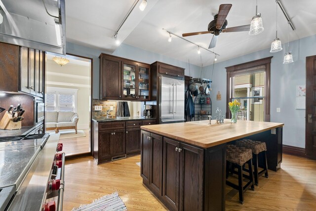 kitchen with a sink, dark brown cabinets, built in refrigerator, light wood-type flooring, and backsplash