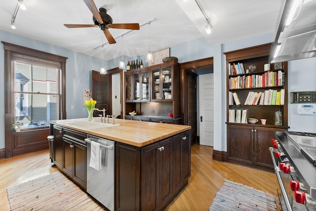 kitchen with dark brown cabinets, butcher block counters, light wood-type flooring, appliances with stainless steel finishes, and a sink