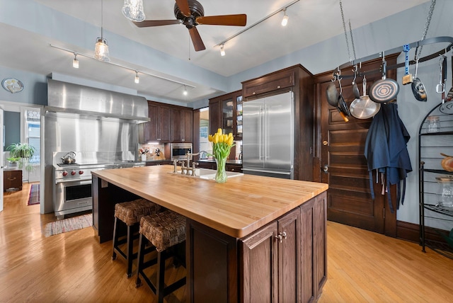 kitchen featuring light wood-type flooring, high quality appliances, an island with sink, a sink, and wood counters