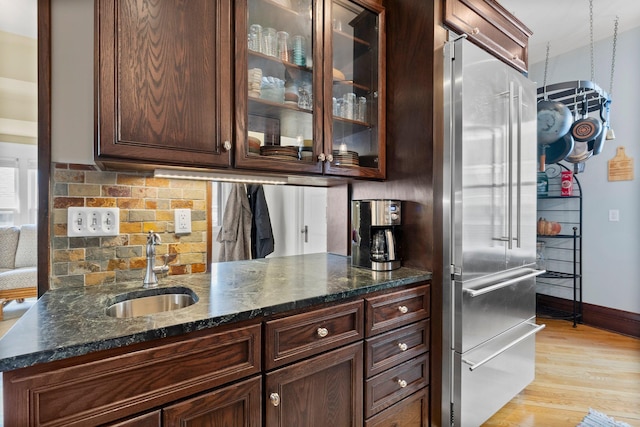 bar with backsplash, baseboards, light wood-style flooring, high end fridge, and a sink