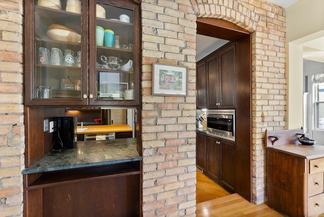 bar featuring stainless steel microwave, light wood-style flooring, and brick wall