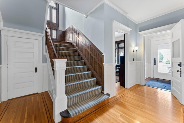 foyer featuring stairway, wainscoting, light wood-type flooring, and ornamental molding