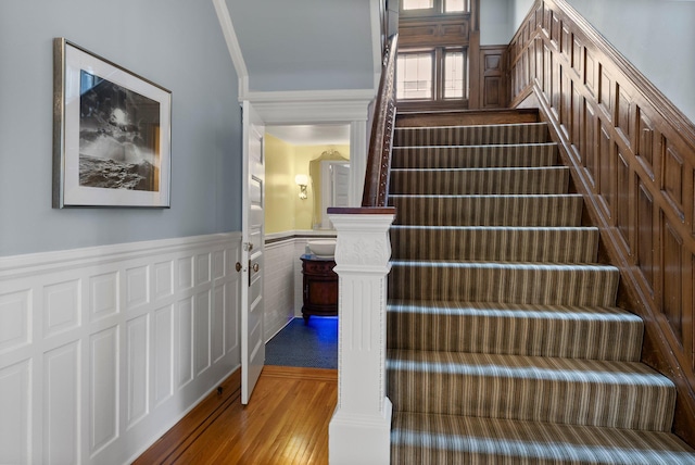 staircase featuring a wainscoted wall, wood finished floors, and crown molding