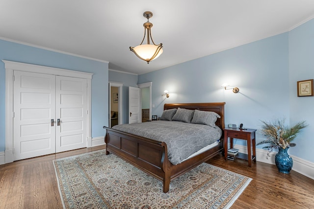 bedroom with crown molding, wood finished floors, baseboards, and a closet