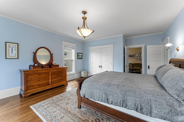 bedroom featuring a closet, baseboards, wood finished floors, and crown molding