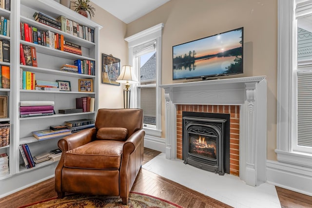 sitting room featuring baseboards, a brick fireplace, and wood finished floors