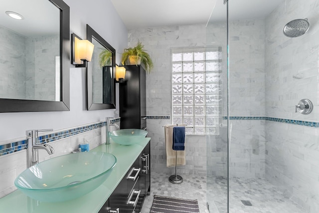 bathroom with tile walls, double vanity, a stall shower, and a sink