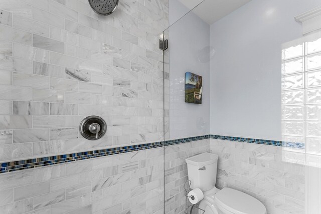 full bathroom featuring tile walls, toilet, a wainscoted wall, and a tile shower