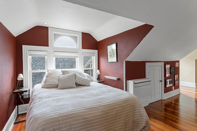 bedroom with a textured wall, baseboards, wood finished floors, and vaulted ceiling