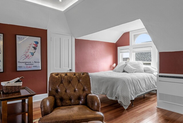 bedroom featuring lofted ceiling, wood finished floors, baseboards, and a textured wall