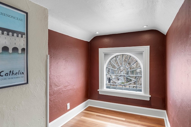 interior details featuring wood finished floors, a textured wall, and baseboards