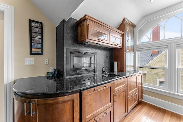 kitchen with vaulted ceiling, light wood-style flooring, dark stone counters, and a sink