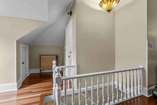 hall with wood finished floors, baseboards, a textured wall, lofted ceiling, and an upstairs landing