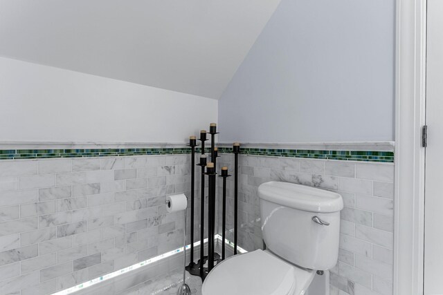 bathroom featuring toilet, tile walls, wainscoting, and vaulted ceiling