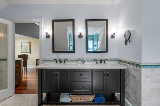 full bathroom with a sink, tile walls, wood finished floors, and double vanity