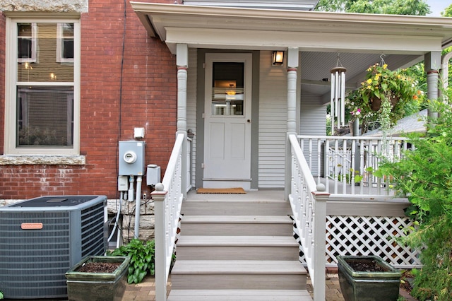 doorway to property with covered porch, brick siding, and central AC