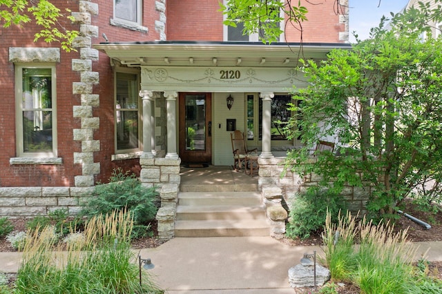 doorway to property with covered porch and brick siding