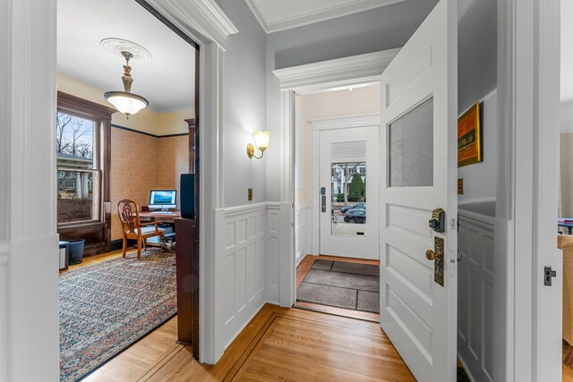 foyer featuring light wood finished floors, wainscoting, ornamental molding, and a decorative wall