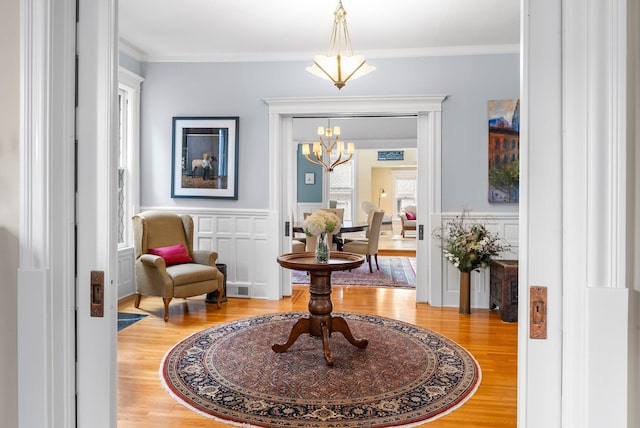 sitting room with light wood finished floors, wainscoting, visible vents, a notable chandelier, and crown molding