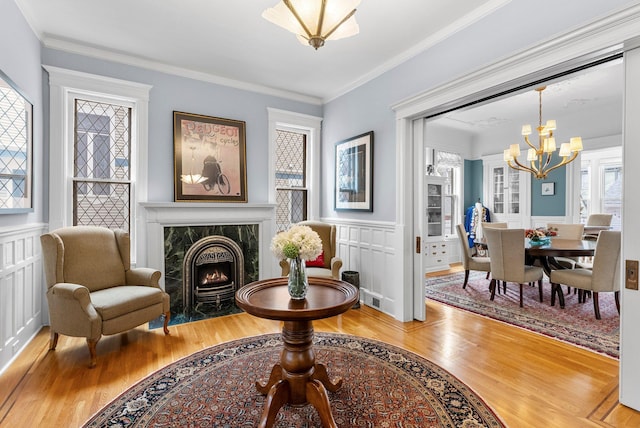 sitting room with wainscoting, a premium fireplace, light wood-style flooring, and an inviting chandelier