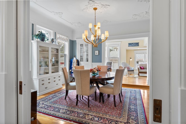dining area featuring light wood-style flooring, a decorative wall, wainscoting, and an inviting chandelier