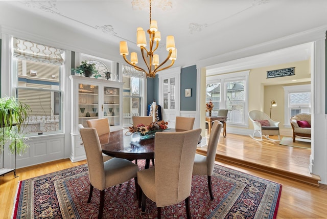 dining space with a chandelier, a decorative wall, light wood finished floors, and wainscoting