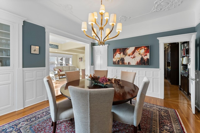 dining space featuring a wainscoted wall, an inviting chandelier, light wood-style flooring, and a decorative wall