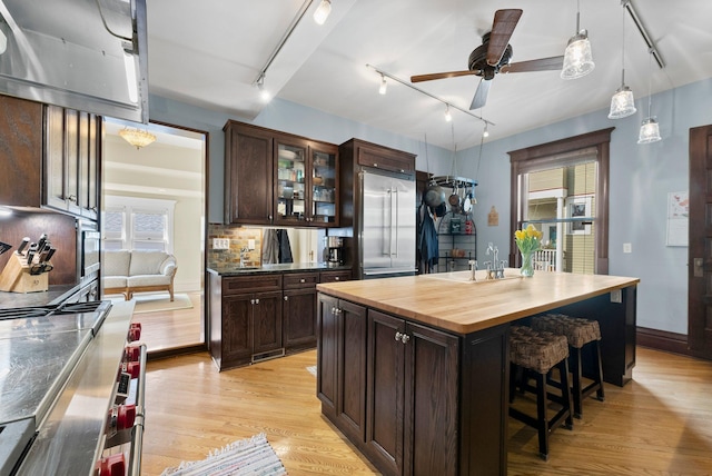kitchen featuring built in fridge, track lighting, dark brown cabinetry, and a sink