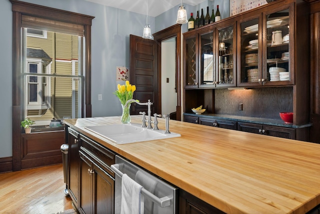bar with light wood-type flooring, stainless steel dishwasher, decorative light fixtures, and a sink