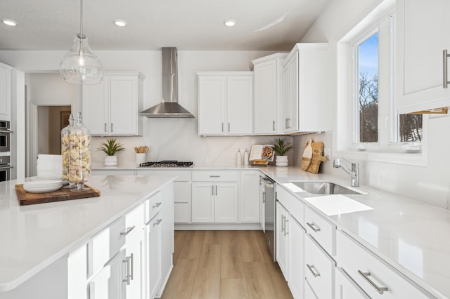 kitchen featuring stainless steel appliances, light countertops, wall chimney range hood, white cabinetry, and a sink