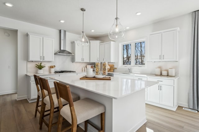 kitchen featuring a breakfast bar, a kitchen island, visible vents, wall chimney range hood, and stainless steel gas stovetop