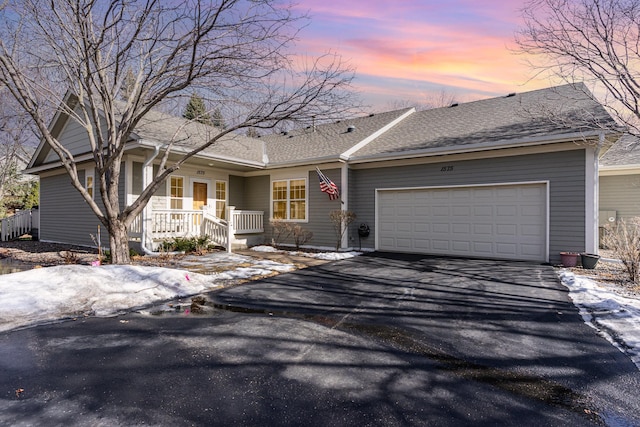 ranch-style home featuring a garage, aphalt driveway, covered porch, and a shingled roof