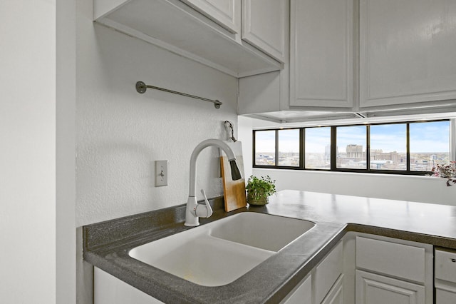 kitchen with a textured wall, a sink, white cabinets, a view of city, and dark countertops