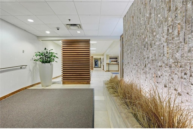 hall with baseboards, visible vents, and a drop ceiling