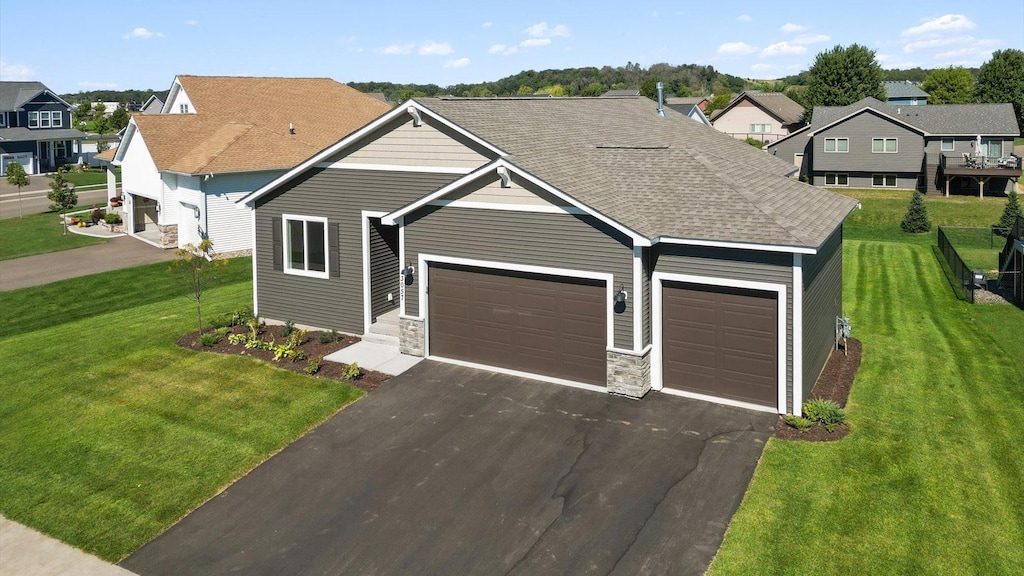 view of front of home with an attached garage, a shingled roof, stone siding, driveway, and a front lawn