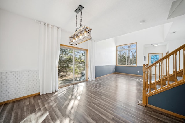 unfurnished dining area with baseboards, stairway, wood finished floors, and wallpapered walls