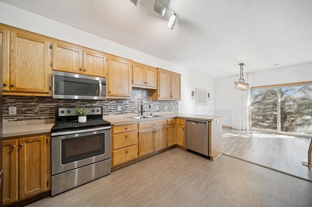 kitchen featuring stainless steel appliances, light countertops, a sink, and a peninsula