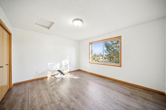 unfurnished room with attic access, a textured ceiling, baseboards, and wood finished floors