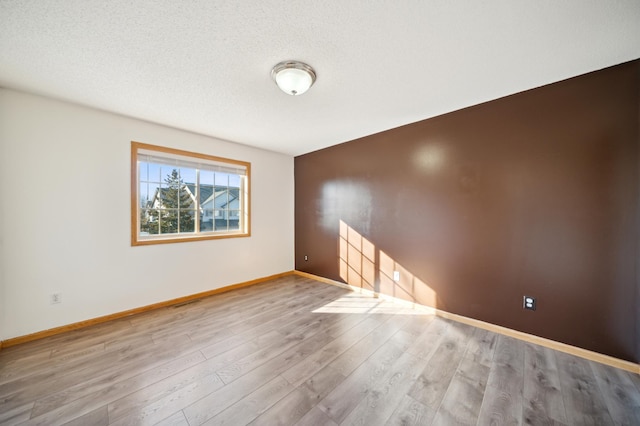 spare room featuring a textured ceiling, baseboards, and wood finished floors