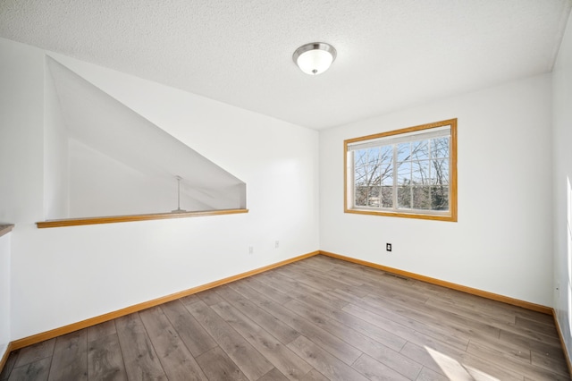 unfurnished room featuring a textured ceiling, baseboards, and wood finished floors