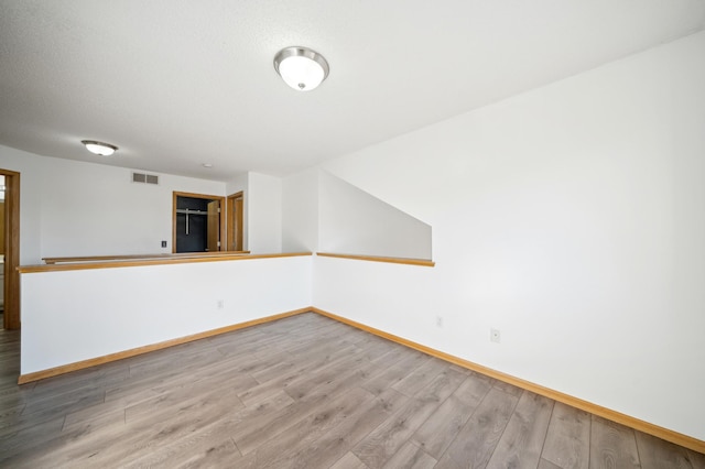 unfurnished room with a textured ceiling, wood finished floors, visible vents, and baseboards