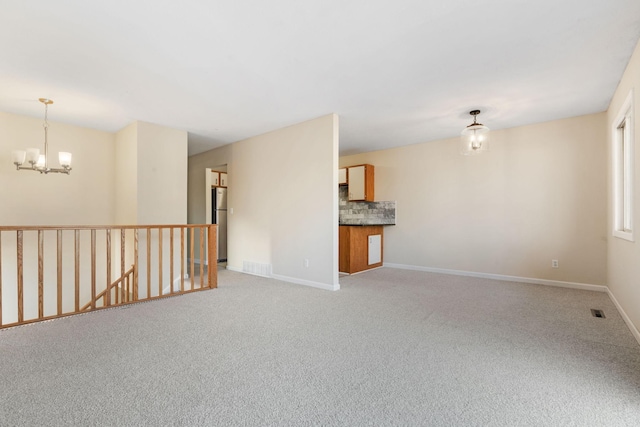 empty room with a chandelier, light colored carpet, visible vents, and baseboards