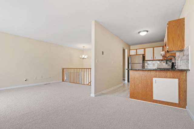 kitchen with dark countertops, light colored carpet, decorative backsplash, freestanding refrigerator, and a chandelier