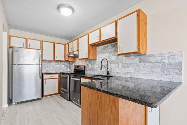 kitchen with stainless steel appliances, backsplash, a sink, dark stone countertops, and under cabinet range hood