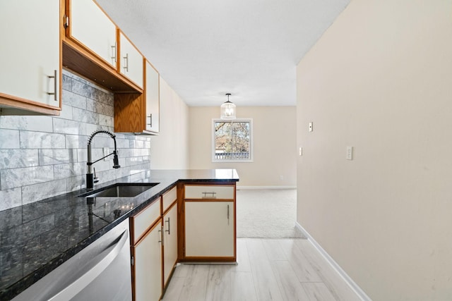 kitchen with a peninsula, a sink, baseboards, stainless steel dishwasher, and tasteful backsplash