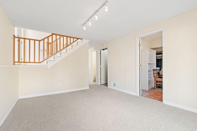 carpeted spare room with stairs, rail lighting, visible vents, and baseboards